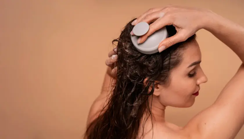 Kvinna med slitet hår använder en scalp massager för att stimulera hårbotten.