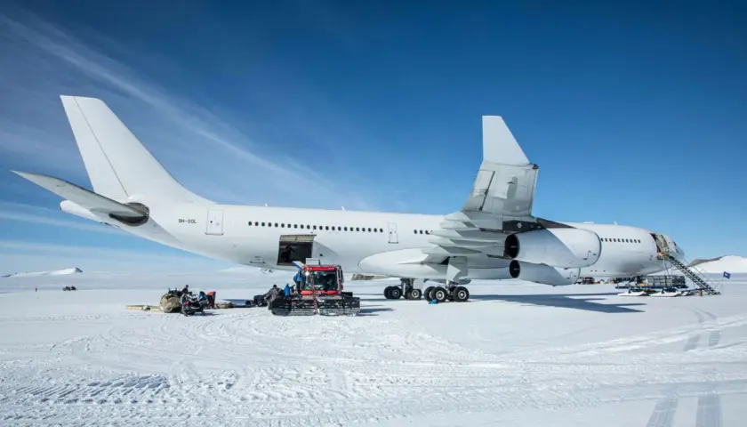 Biały airbus a340-300 na śniegu, z obsługą naziemną i ratrakiem.