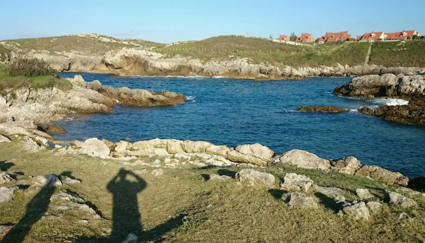 La **playa de Canallave** se asoma entre rocas y aguas turquesas. En la colina, casas de tejados rojos vigilan el mar.