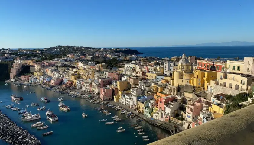 Vue panoramique de Procida ou Ischia, avec ses maisons colorées nichées sur la côte et des bateaux dans le port.