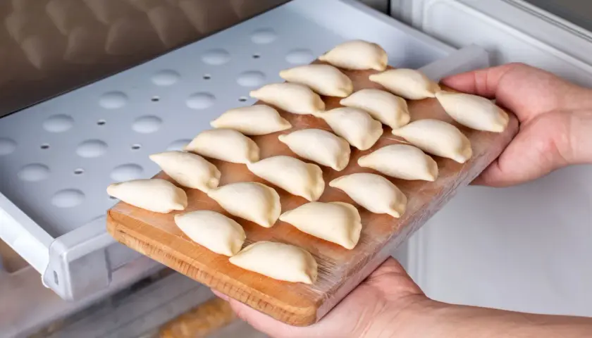 Ręce wkładają deskę z surowymi pierogami do zamrażarki. To prosty sposób, jak przechować ciasto na pierogi na później.