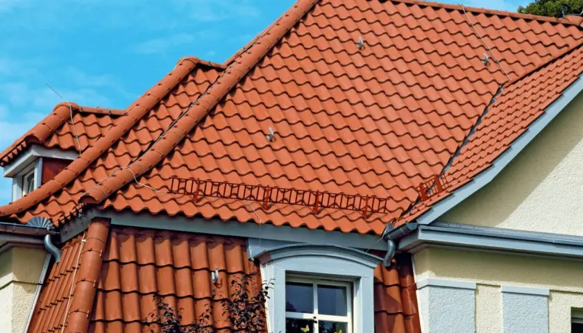 Dwa rodzaje dachów z czerwonej dachówki ceramicznej, jeden płaski, drugi skośny, pod błękitnym niebem.