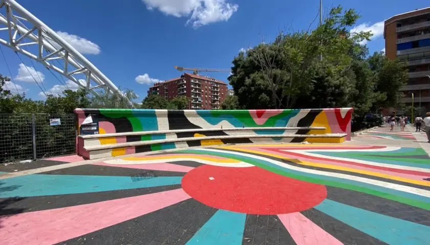 Piazza colorata vicino alla metro Garbatella a Roma, con un murale vivace e un grande sole stilizzato sul pavimento.