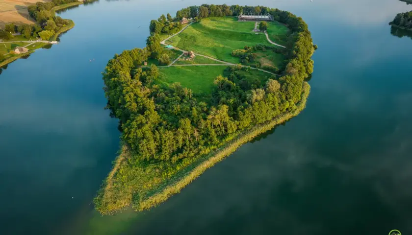 Gniezno gród zwiedzanie: malownicza wyspa z historycznymi zabudowaniami i zielonymi terenami, otoczona wodą.