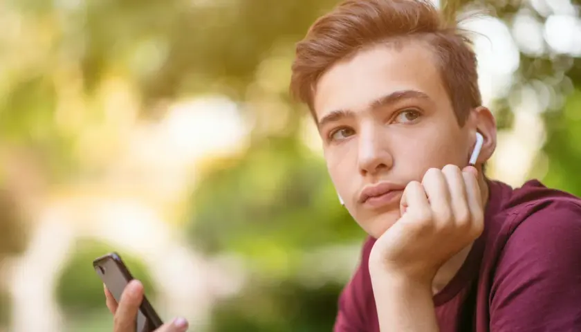 Chłopak z telefonem i słuchawkami zastanawia się, o czym rozmawiać z dziewczyną przez telefon.