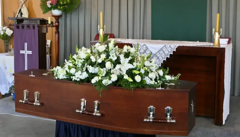 Drewniana trumna ozdobiona białymi kwiatami, symbolizująca pożegnanie zmarłego.