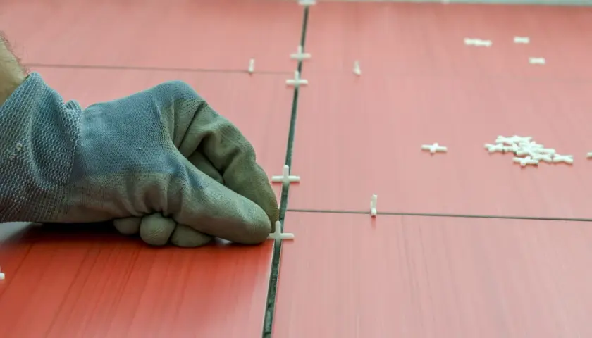 Main tenant, ganté, ajuste des croisillons pour refaire le joint du carrelage rouge.