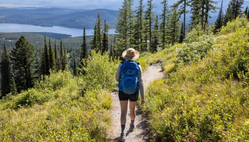 A hiker with a blue backpack walks on a trail, enjoying one of the best long hikes in the world with a stunning lake and mountain view.