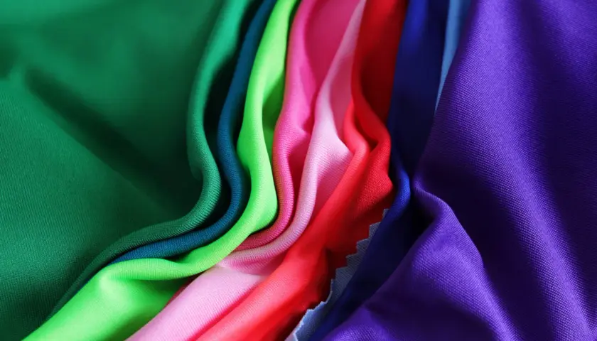 A vibrant collection of athletic wear fabric swatches in green, teal, lime, pink, red, blue, and purple, draped and folded.