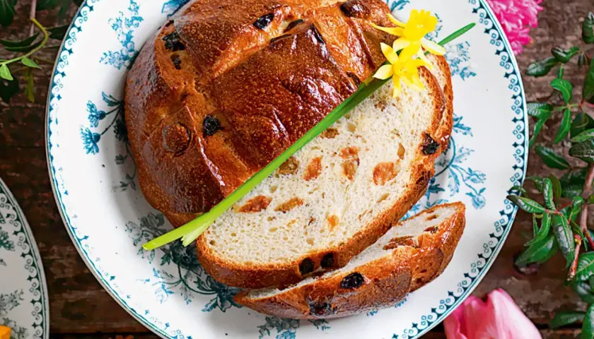Pan di ramerino dorato, con uvetta e scorze candite, guarnito con un fiore giallo e un rametto verde.