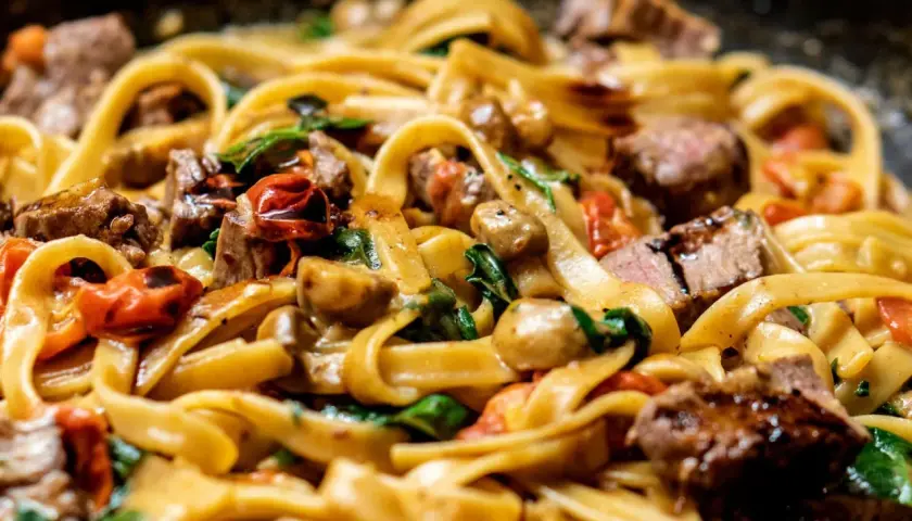 Un plat de pâtes tagliatelles avec des morceaux de bœuf, des tomates cerises et des champignons. Une excellente idée recette pâtes pour un repas savoureux.