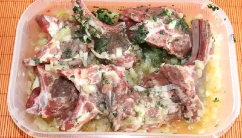 Côtelettes d'agneau crues dans une marinade à l'oignon et aux herbes, prêtes pour une recette de marinade agneau barbecue.
