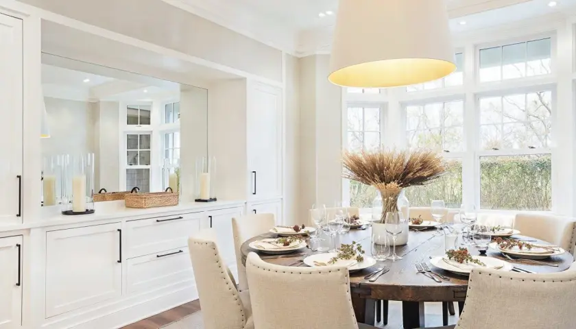 Elegant dining room inspiration featuring a rustic wooden table set for a meal, surrounded by upholstered chairs. Large windows offer a view of nature.