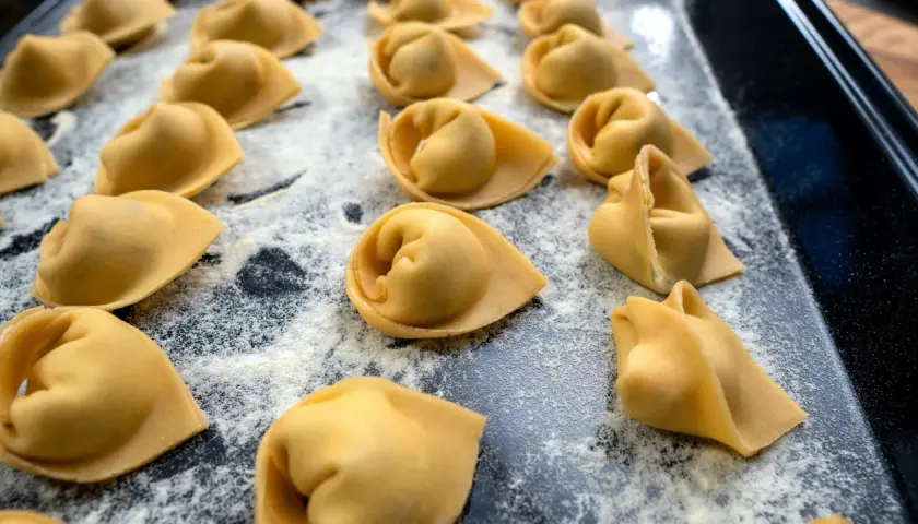 Frisch geformte Tortellini liegen auf einer bemehlten Fläche. Das Selbermachen von Tortellini ist ein Genuss für alle Sinne.