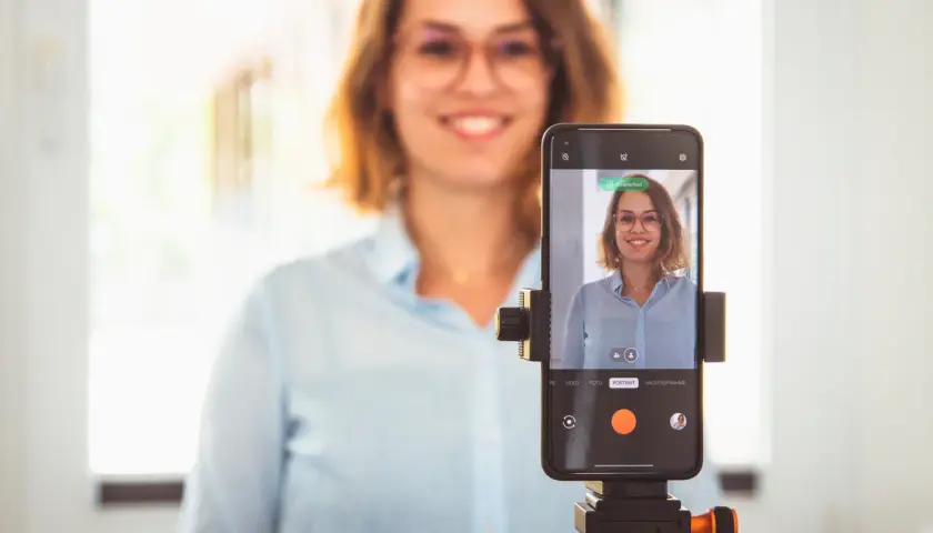 Frau macht ein bewerbungsfoto selber machen mit dem Handy auf einem Stativ.