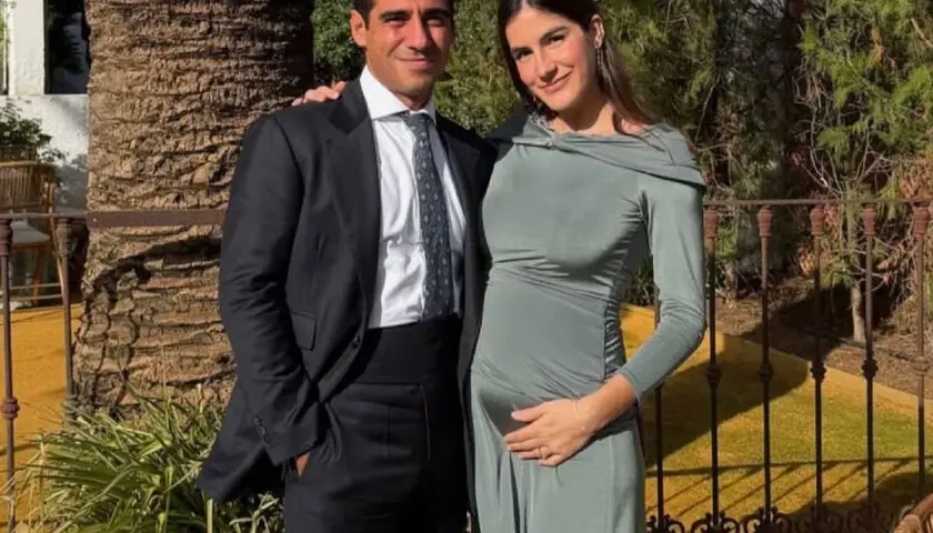 Pareja sonriente, él con traje oscuro, ella con vestido verde ceñido, acariciando su vientre. Blanca Llandres, radiante, espera un bebé.