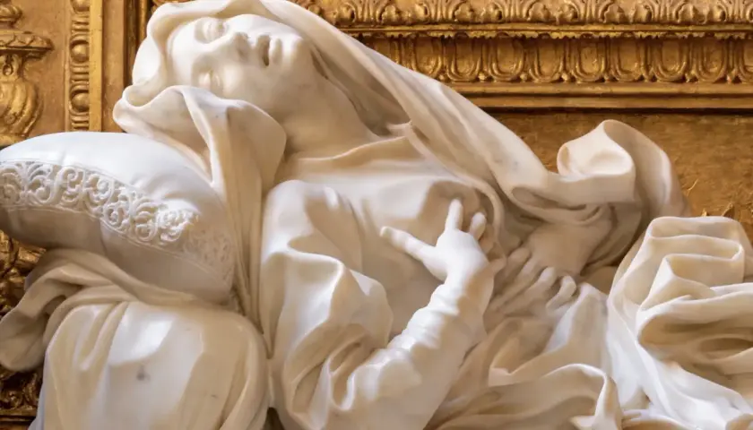 Scultura in marmo di Santa Teresa in estasi, capolavoro barocco a Roma. La sua mano sfiora il petto, mentre il volto esprime un profondo trasporto spirituale.
