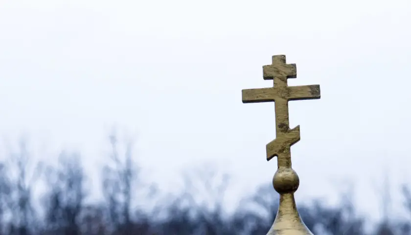 Złoty krzyż prawosławny na tle pochmurnego nieba. Symbolizuje nadzieję i pamięć podczas pogrzebu prawosławnego.