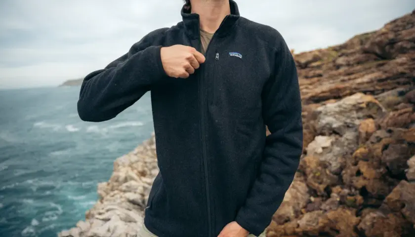 A man zips up a dark grey sweater fleece jacket, perfect for a coastal adventure. The textured fabric offers warmth and comfort.