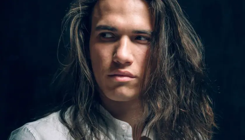 Joven con cabello largo y castaño, con un estilo que resalta el cuidado del cabello hombre.