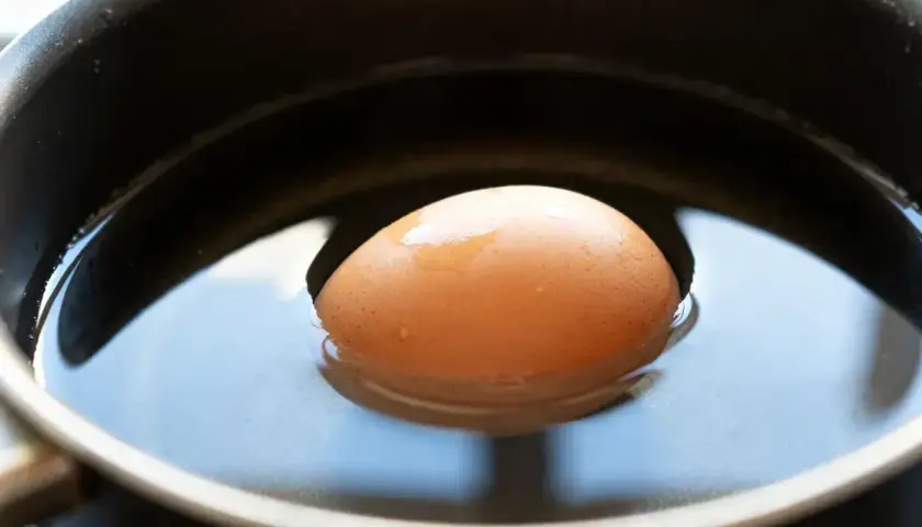 Un œuf frais flotte dans l'eau d'une casserole, prêt à être cuit.