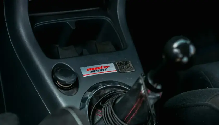 Wnętrze samochodu z naklejką "Monster Sport" i gniazdem zapalniczki. Który bezpiecznik jest od zapalniczki?
