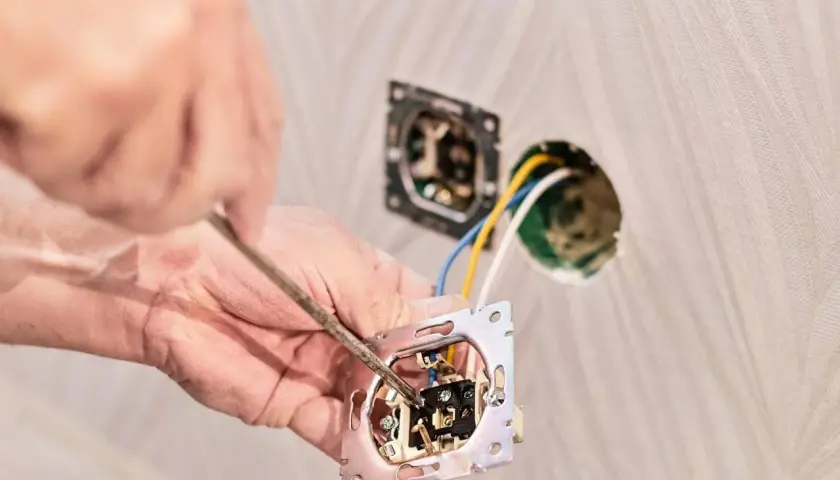 Instalator podłącza włącznik światła podwójny trzy przewody. Widać rękę z wkrętakiem i mechanizm włącznika.