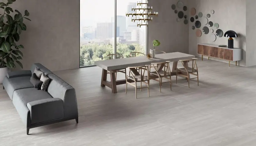 Un elegante soggiorno con divano grigio, tavolo da pranzo in cemento e sedie in legno, il tutto su un pavimento in gres porcellanato ruvido che evoca un'atmosfera moderna e accogliente.