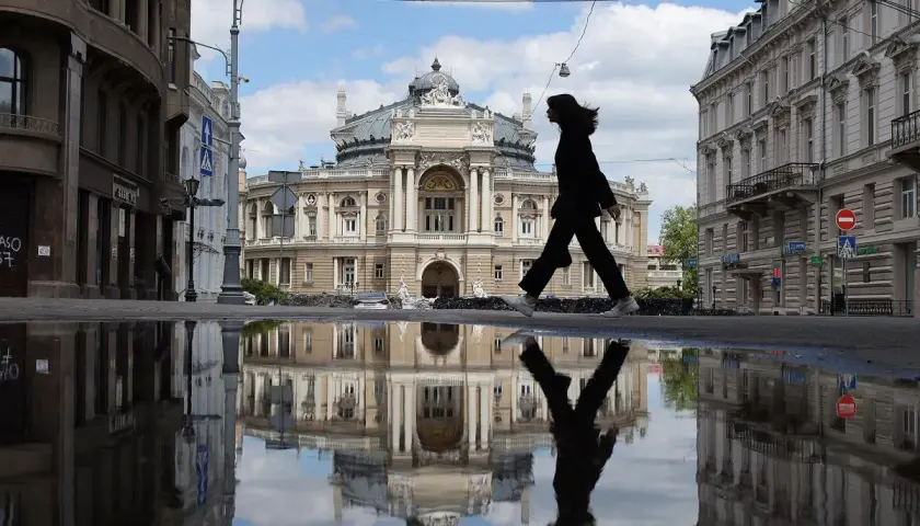 Kobieta idzie przez kałużę przed Teatrem Opery i Baletu w Odessie, tworząc odbicie niczym z filmu.