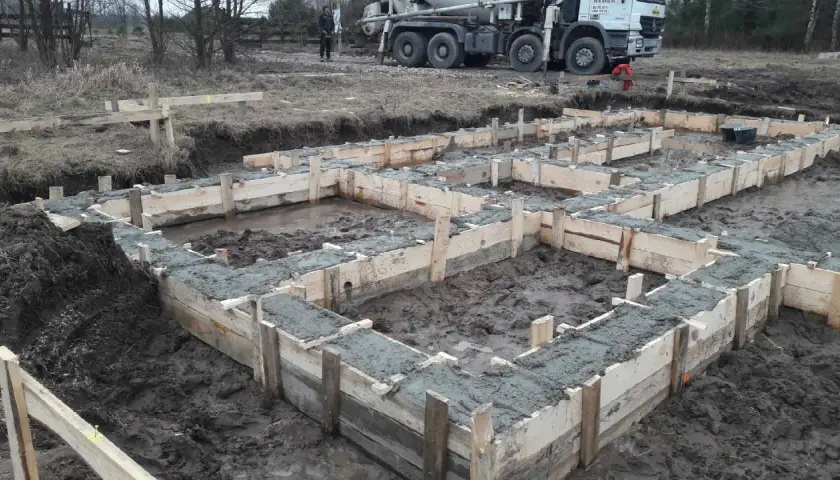 Rozpoczęła się budowa domu drewnianego. Wylano fundamenty, widać drewniane szalunki i świeży beton. W tle stoi gruszka z betonem.