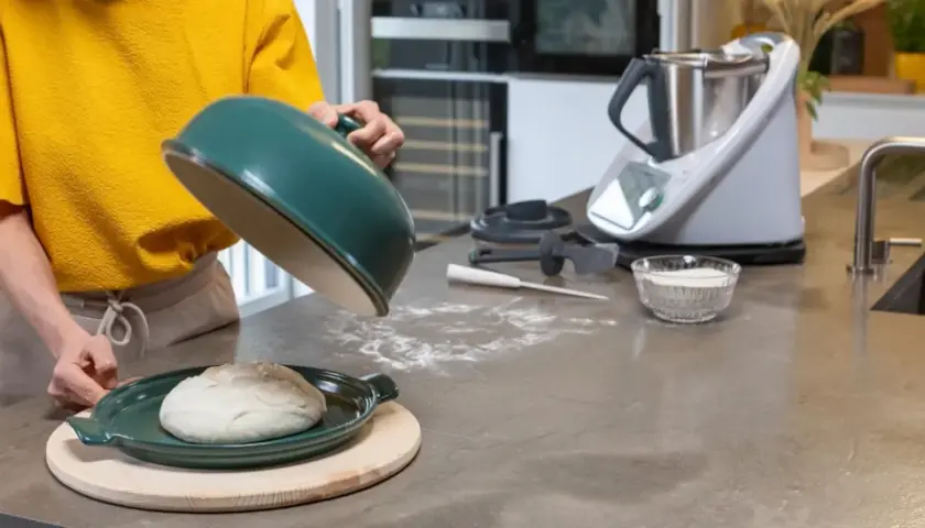 Préparation de la pâte à pizza avec un robot culinaire. Une boule de pâte repose sur un plat vert, prête à être cuite.