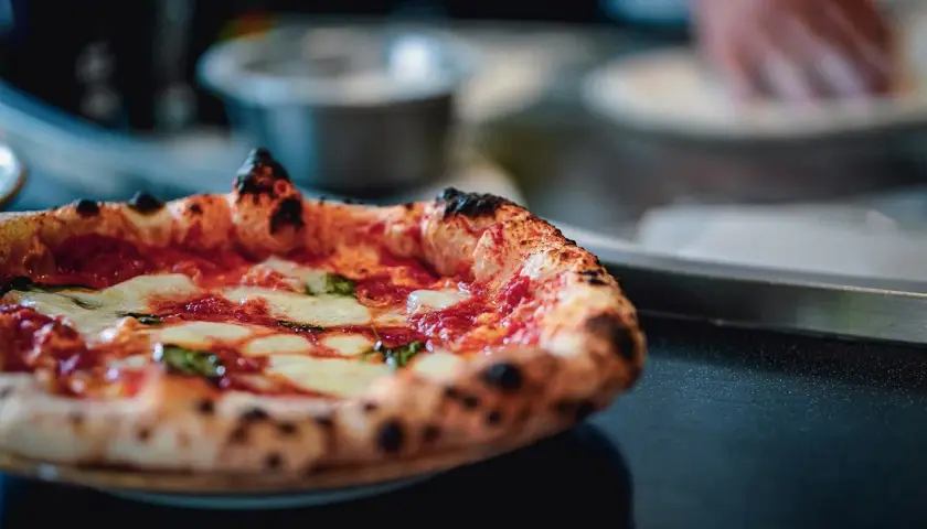 Puszysta pizza z serem i bazylią na ciemnym tle.