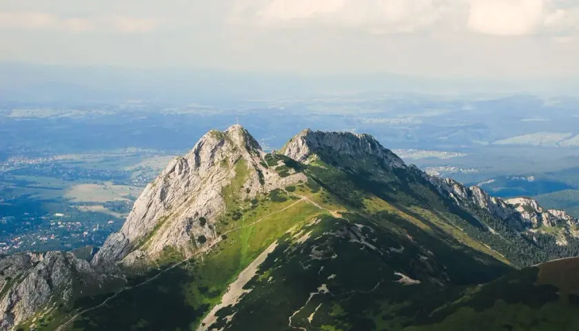 Górskie szczyty z zielonymi zboczami i kamienistymi graniami, w oddali widać dolinę i chmury.