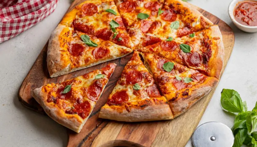 Krojona pizza pepperoni z serem i bazylią na drewnianej desce.