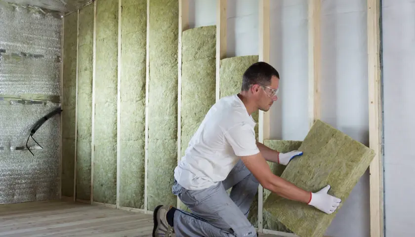 Un ouvrier installe un panneau d'isolant thermique dans une structure murale en bois.
