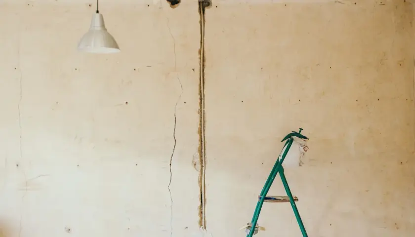 Pękające ściany starego domu, widoczna instalacja elektryczna i drabina.