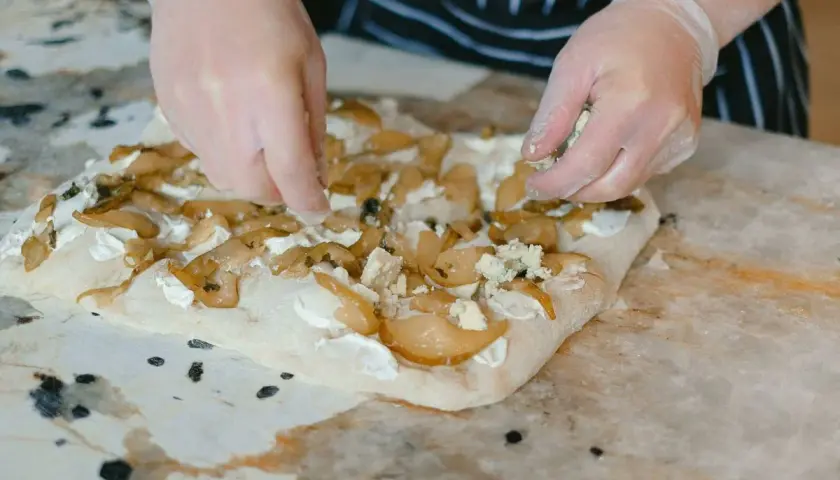 Manos enguantadas añaden queso azul a una focaccia con peras. Una deliciosa focaccia reteta en proceso.