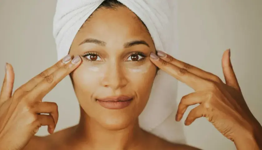 Mujer con toalla en la cabeza aplica crema con ceramida alrededor de sus ojos.