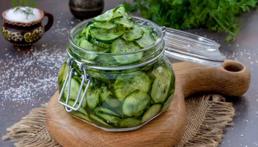 Barattolo di vetro pieno di fette di cetrioli in agrodolce, con aneto e sale sparso.