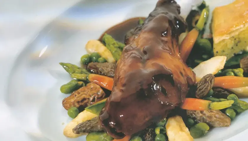 Ein köstliches Kaninchen-Rezept: zartes Kaninchenfleisch in dunkler Sauce, serviert mit Spargel, Erbsen, Karotten und Morcheln.