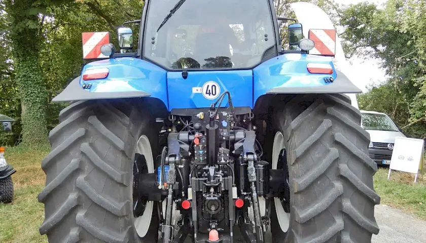Blauer Traktor mit großen Reifen. An der Seite sind rot-weiße Warnschilder mit Beleuchtung angebracht.