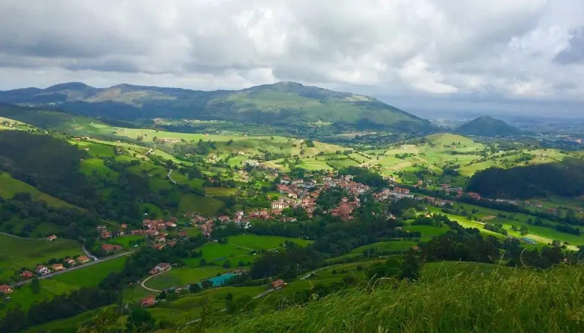 Paisaje verde y montañoso, con un pueblo en el valle. La **ruta Tetas de Liérganes** ofrece vistas espectaculares.