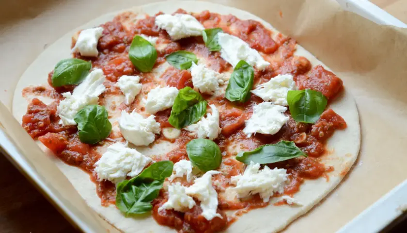 Pizza mozzarella z pomidorami i bazylią, gotowa do pieczenia.