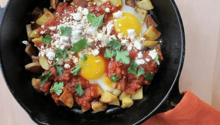 Plat savoureux : recette pomme de terre oeuf avec sauce tomate, fromage émietté et persil frais, servi dans une poêle en fonte.