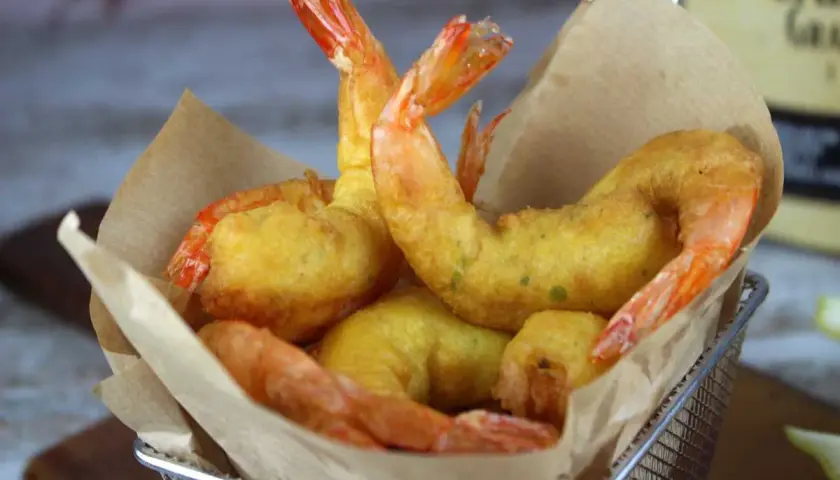 Crujientes gambas a la gabardina doradas, servidas en una cesta metálica con papel marrón.