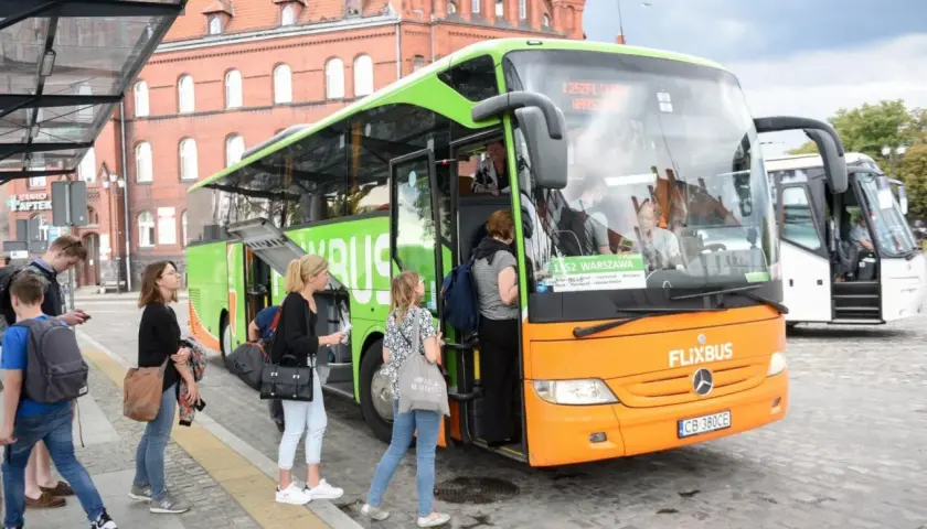 Pomarańczowo-zielony autobus FlixBus na przystanku, pasażerowie wsiadają.