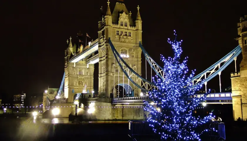 Albero di Natale illuminato con luci blu davanti al Tower Bridge di Londra, evocando l'atmosfera dei mercatini di Natale in inglese.