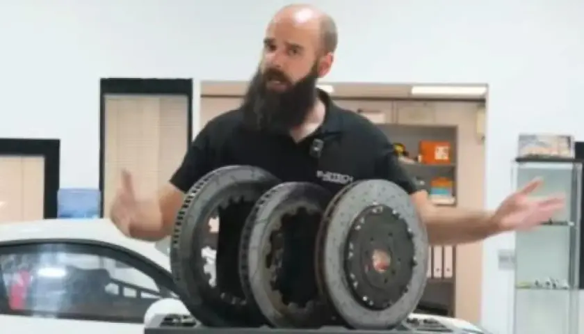 Hombre con barba muestra tres discos de freno, uno de ellos con perforaciones, para mejorar la refrigeración en un coche deportivo.