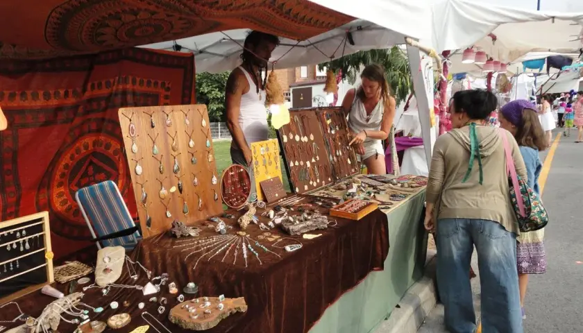 En el **mercado hippie Argaños**, se exhiben collares y pulseras artesanales. Una vendedora muestra su mercancía a dos clientas.