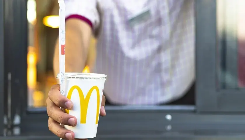 Ręka podaje kubek z McDonald's. Zastanawiasz się, ile kalorii ma cola zero z McDonald's? Ten napój ma zero kalorii.